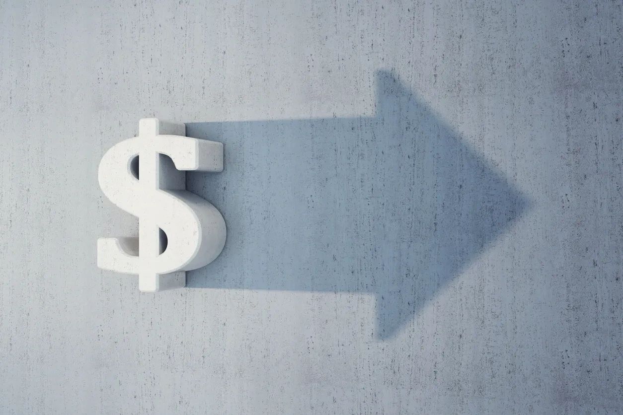 Dollar sign casting a shadow shaped like an arrow on a textured wall.