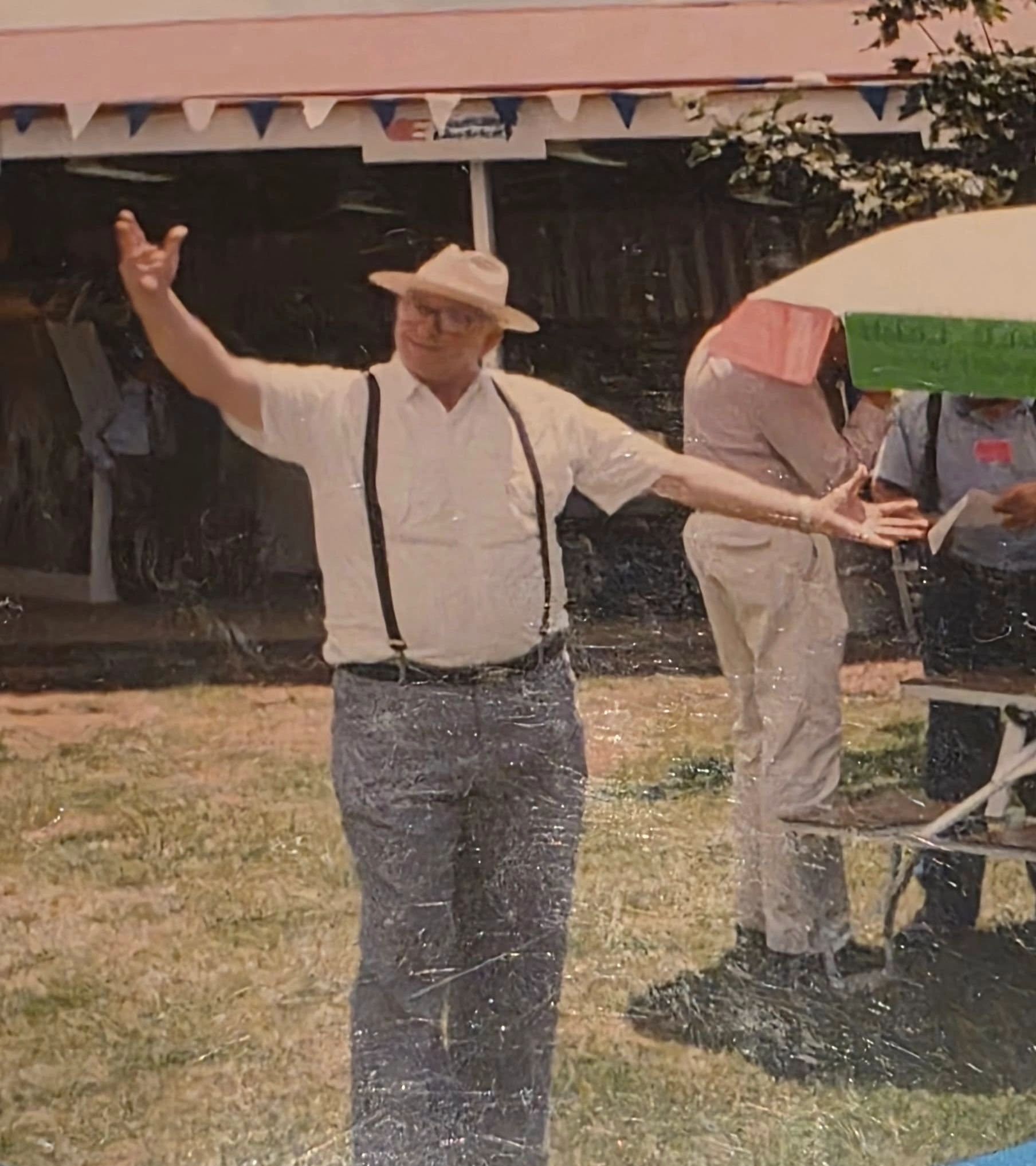 Man in hat dancing outdoors with suspenders.