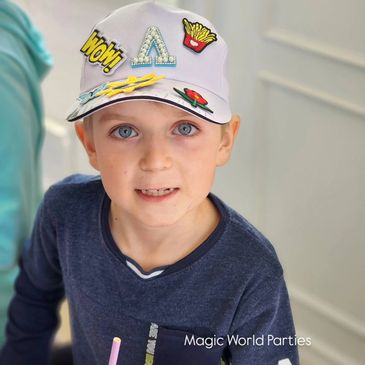 Young boy wearing a decorated white cap and a navy blue shirt.