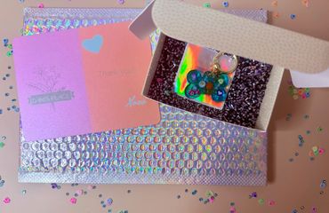 A colorful keychain in a box with thank you cards and holographic packaging.