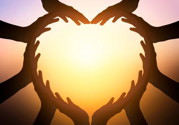 Multiple hands forming a heart shape against a sunset background.