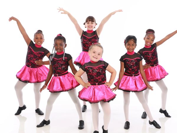 Group of young girls in pink and black dance costumes posing.