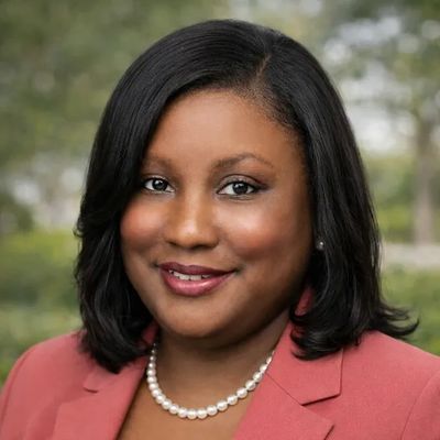 Professional woman smiling, wearing a coral blazer and pearl necklace.