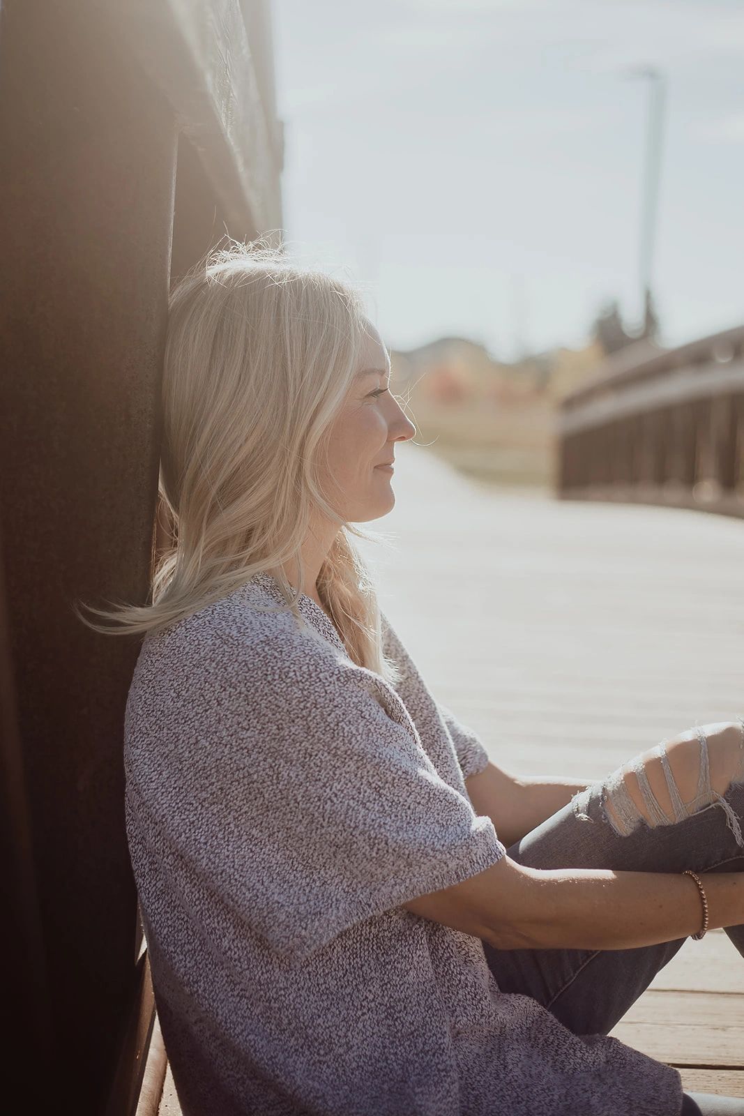 Woman sitting peacefully on a wooden bridge in sunlight.