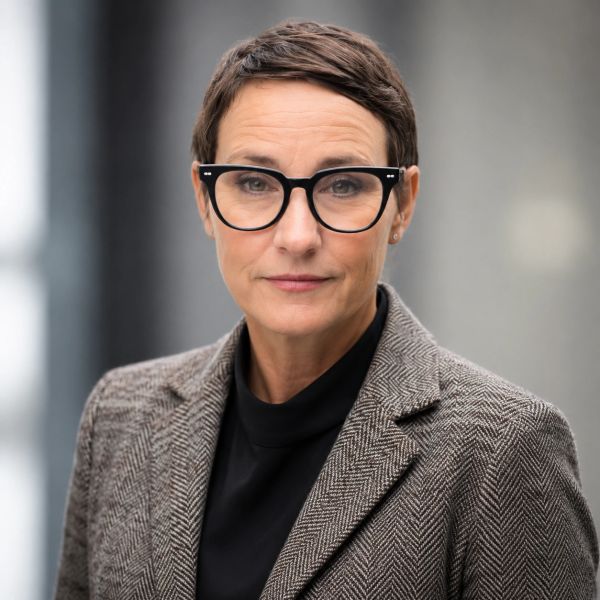 Professional woman with short hair and glasses wearing a tweed blazer.