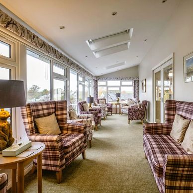 A bright and airy conservatory with neutral coloured carpet is stylish purple chequered armchairs