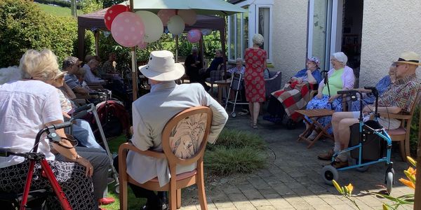A group of people enjoying the garden together. Some have walking frames or wheelchairs