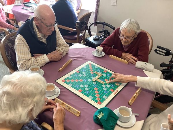 Four people playing a game of scrabble while enjoying cups of tea