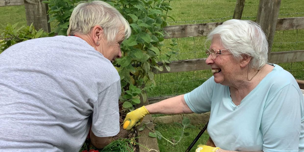 Two ladies gardening together, smiling at each other