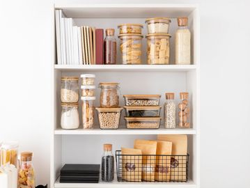 A neatly organised kitchen cupboard with food items decanted into jars