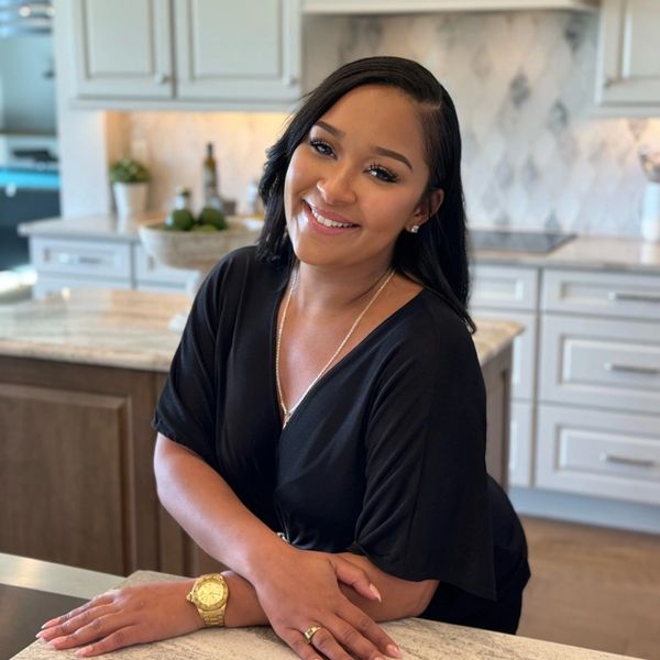 Smiling woman in a black dress leaning on a kitchen counter.