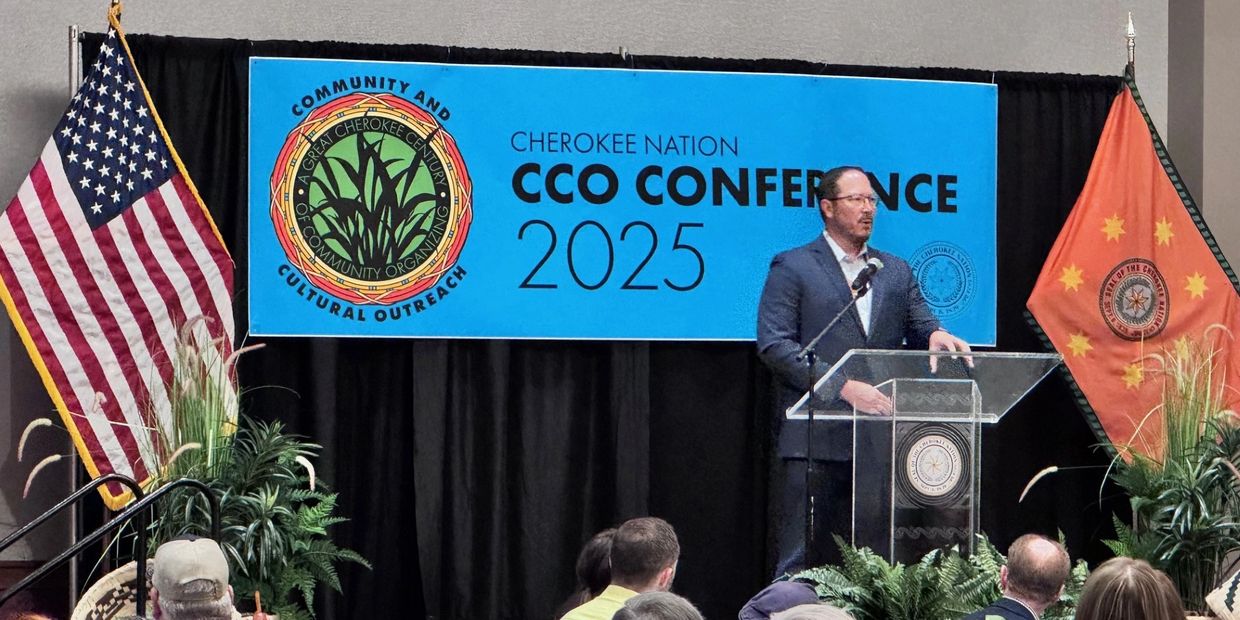 Speaker at the Cherokee Nation CCO Conference 2025 with flags and audience.