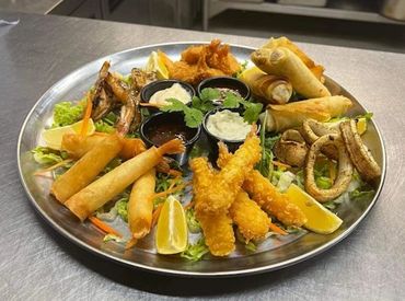 A platter of assorted fried appetizers with dipping sauces and lemon wedges.
