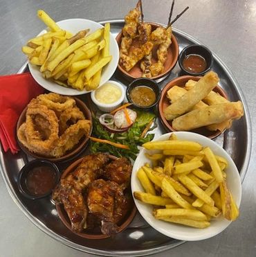 A platter with fries, onion rings, chicken skewers, spring rolls, ribs, and dipping sauces.