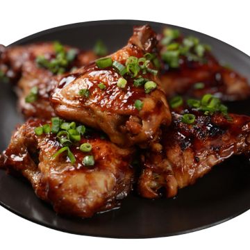 Glazed chicken wings garnished with chopped green onions on a black plate.