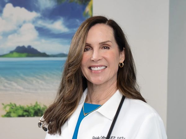 Smiling female healthcare professional in white coat with stethoscope at keyboard.