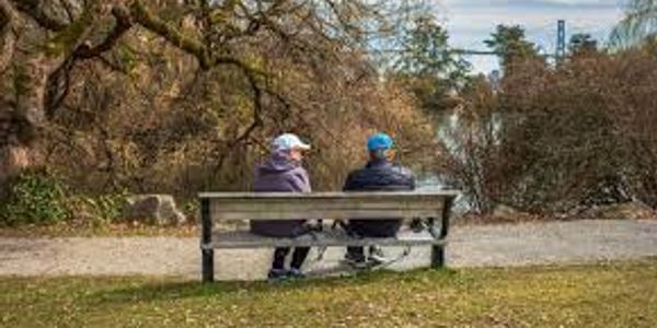 Two people sitting on a bench by a river in a park.