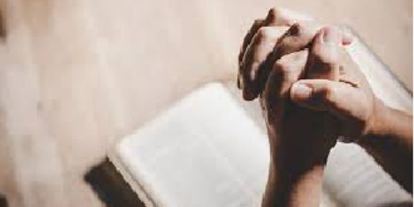 Hands clasped in prayer over an open book, likely a Bible.