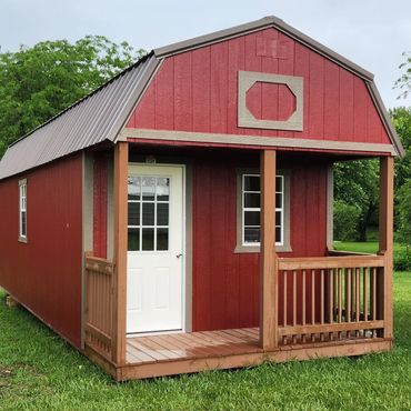 Red tiny house with white door and wooden porch on green grass.
