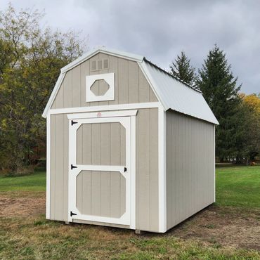 Beige garden shed with white trim on a grassy lawn under a cloudy sky.