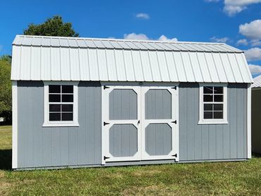 Two garden sheds stand on a grassy lawn under a blue sky.