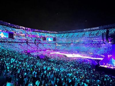 A vibrant concert at MetLife Stadium with colorful lights and a huge crowd.
