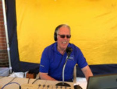 Man in blue shirt wearing headphones speaking into a microphone.