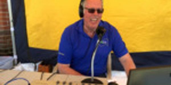 Man in blue shirt wearing headphones speaking into a microphone.