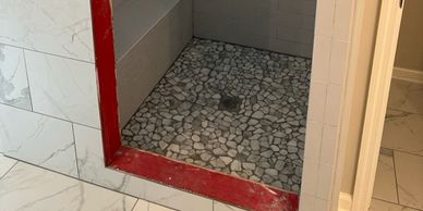 Shower area with pebble stone floor and red frame.