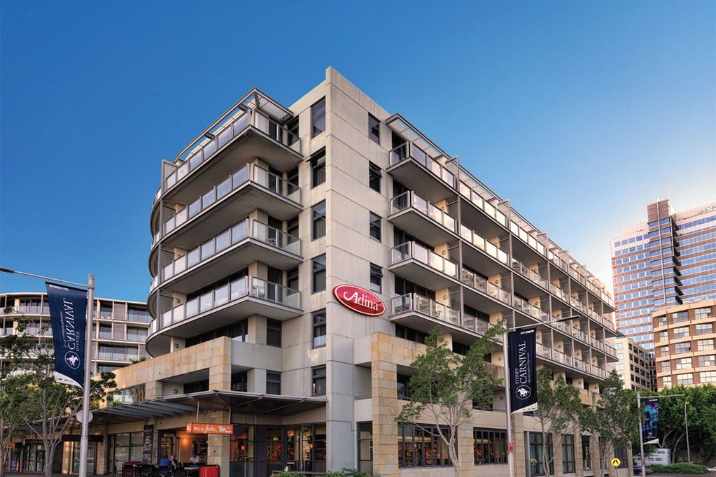Modern multi-story Adina apartment building with balconies under a clear blue sky.