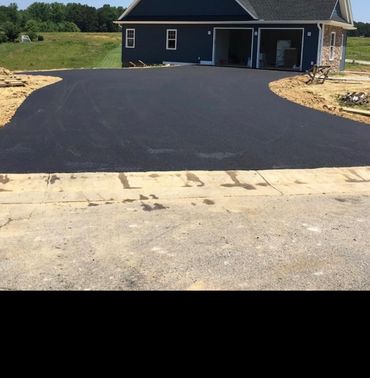 Freshly paved wide black asphalt driveway leading to a two-car garage.