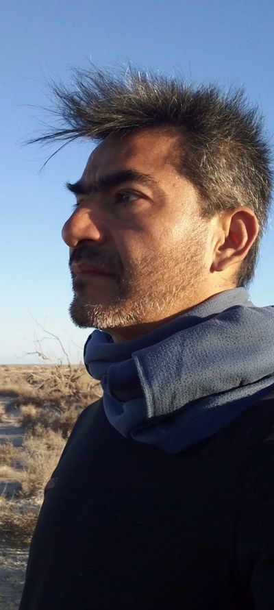 Profile of a man with spiked hair standing outdoors under clear blue sky.