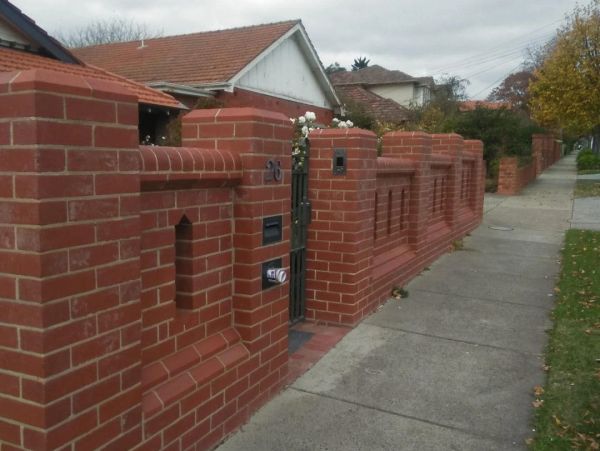 A long red brick fence with decorative pillars along a sidewalk.
