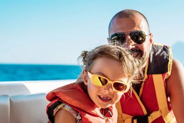 Father and daughter wearing life jackets on a boat under sunny weather.