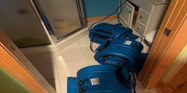 Commercial air movers drying a water-damaged bathroom floor after water extraction