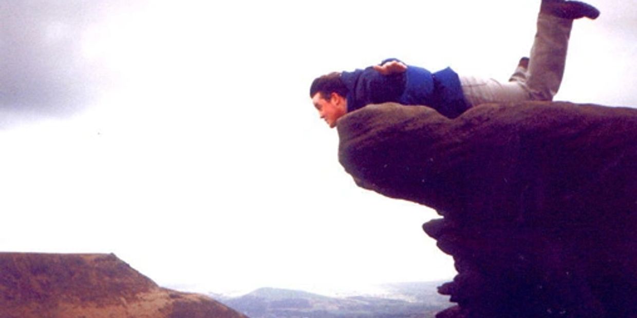 Person lying face down on a rock ledge overlooking a valley.