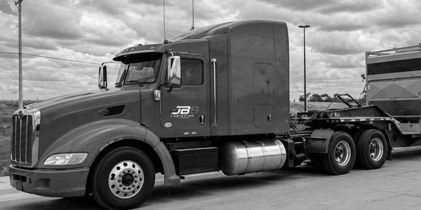 Black and white image of a JB Transport semi truck parked on a paved surface.