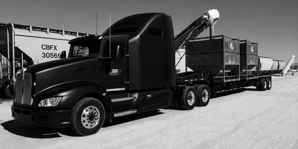 Black semi-truck with a long trailer in an industrial area.