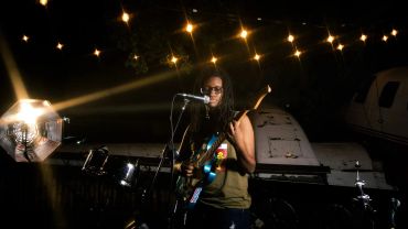 Marz playing guitar and singing on stage with string lights.