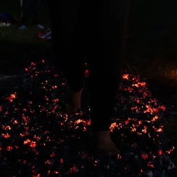 Person walking barefoot on glowing hot coals at night.