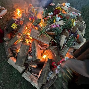 A fire burning with flowers placed on top, surrounded by logs.