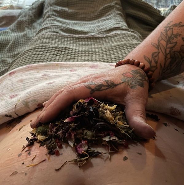 Hand with tattoo holding dried flowers on a stomach.