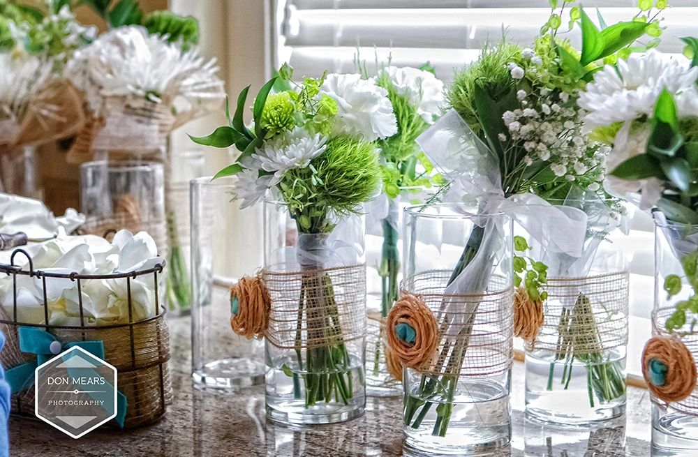 Elegant floral arrangements in clear glass vases with decorative twine and blue accents.