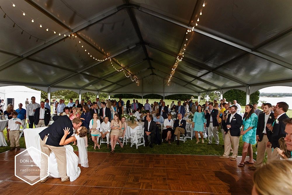 Bride and groom share a kiss during their wedding reception under a large tent.