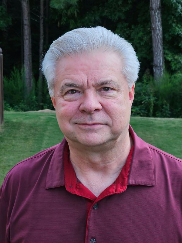 Portrait of a smiling older man with gray hair outdoors.