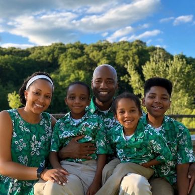 Family of five in matching green floral shirts outdoors.