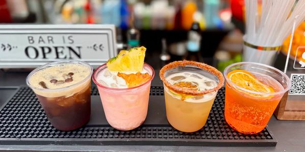 Quatre cocktails colorés alignés au bar.