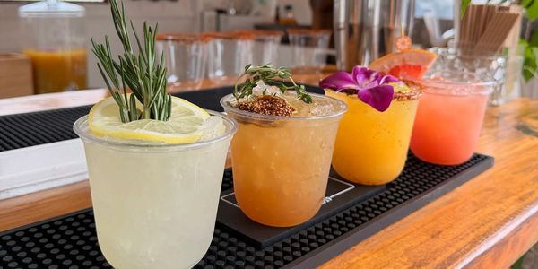 Quatre cocktails colorés alignés sur un bar en bois.