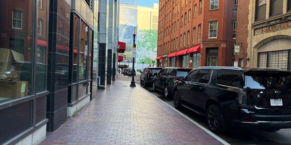 City street with parked black SUVs and brick buildings under clear sky.