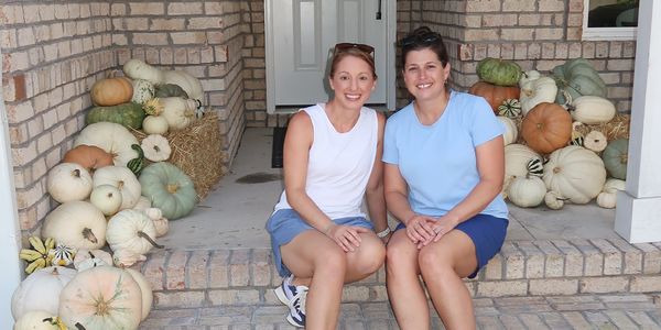 Two women sitting on a porch surrounded by pumpkins.